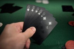 Man holding black playing cards while playing poker.